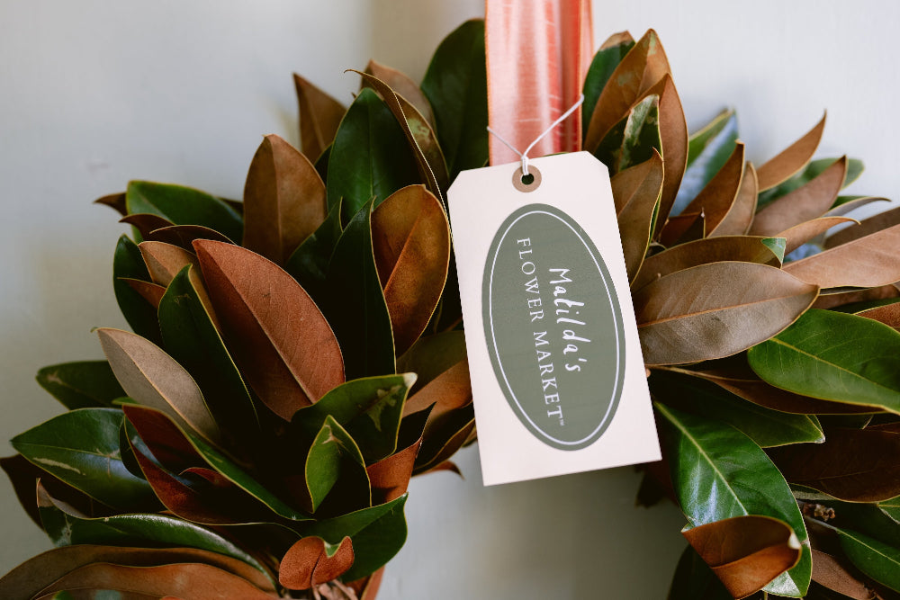 Close-up of farm fresh magnolia wreath with satin ribbon, handcrafted in California by Matilda’s Flower Market.